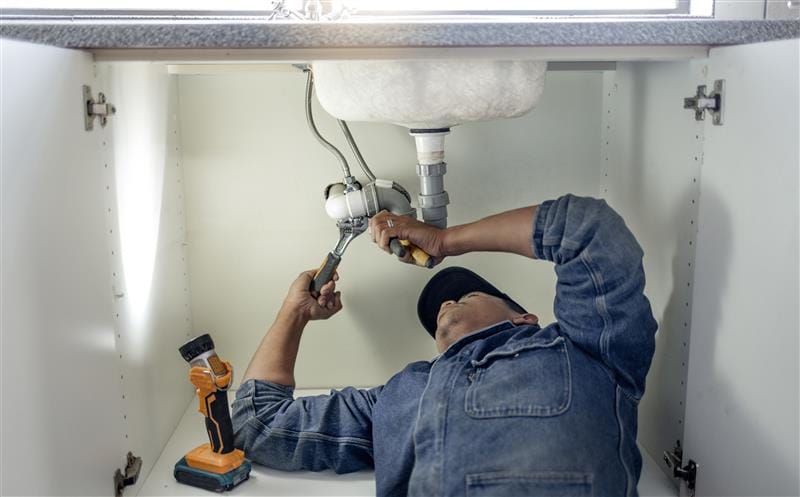Plumber repairing pipes beneath a bathroom sink in Tarpon Springs