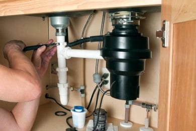 Plumber repairing a garbage disposal beneath a kitchen sink in Tarpon Springs