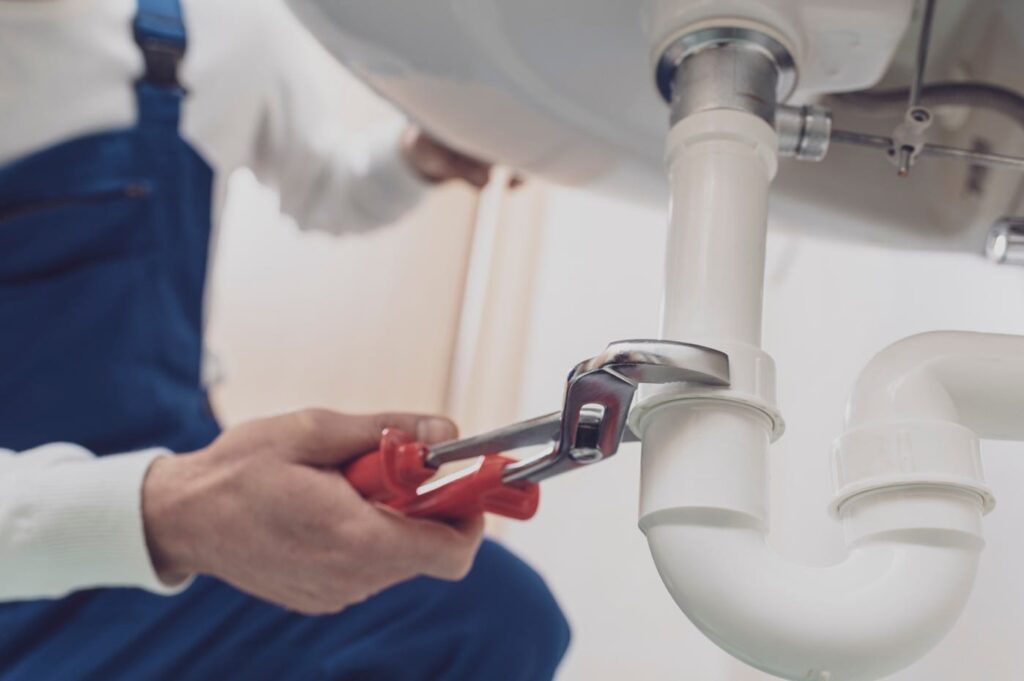 Plumber repairing a white drain pipe beneath a sink in Tarpon Springs